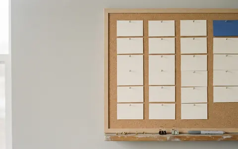 Plain index cards pinned in columns to a cork board, one card in blue, with pins and a marker on the ledge.